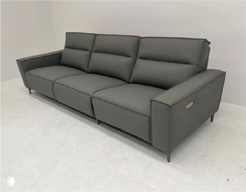 Фото трёхместного серого дивана из кожи в студии: три сиденья, аккуратные швы, тонкие подлокотники и ножки.