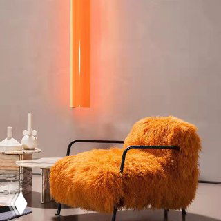 Оранжевое пушистое кресло, обитое тёплой овчиной, с чёрными металлическими подлокотниками на фоне светлого интерьерного фона.