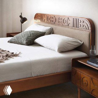 Крупный план изголовья кровати Madrid: резной деревянный декор, обивка в мягкой текстуре, декоративная подушка и настенный светильник.