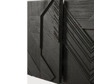 Деталь боковой панели тумбы с резным узором и интегрированной рукоятью, подчёркнуты края и крупная текстура ясеня в чёрной отделке.