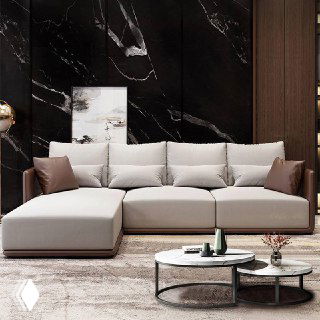 Угловой бежевый диван с оттоманкой и кожаными акцентами, расположенный на фоне тёмной мраморной панели в гостиной.