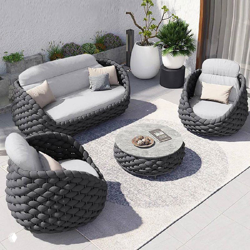 Набор уличной мебели из плетёного ротанга: диван, два кресла и низкий круглый стол на террасе, светло‑серые подушки и декор.