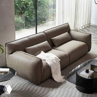 Диван Navola в кожаной обивке, ракурс слева сверху, две декоративные подушки и плед, интерьер с зеленью за окном