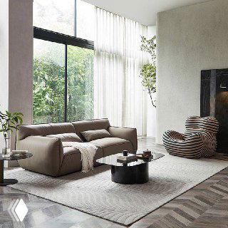 Широкий диван Navola в интерьере с высокими окнами, общий вид на зону отдыха с журнальным столиком и растениями