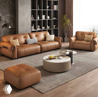 Широкий кожаный диван с креслом и оттоманкой в светлой гостиной: общий ракурс показывает комплект мебели и декоративные элементы на полках.