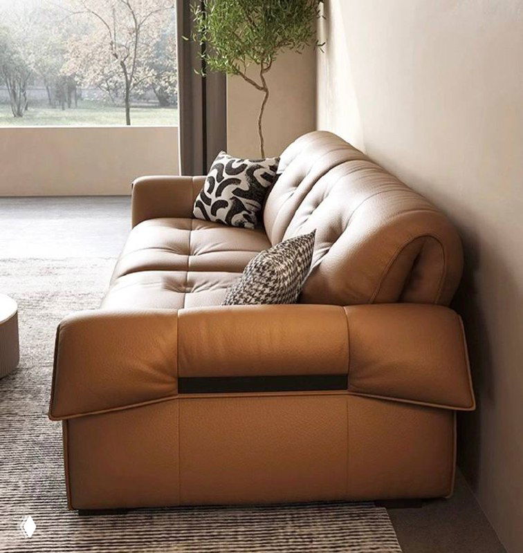 Боковой ракурс кожаного дивана у стены: показана глубина сидений, подлокотники и посадочная глубина в контексте минималистичного интерьера.