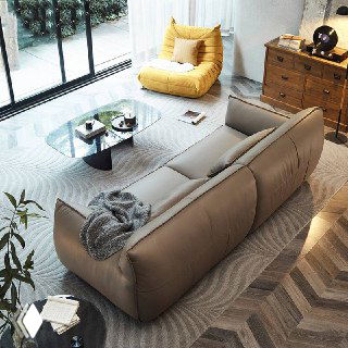 Вид сзади и с угла дивана Navola в кожаной отделке, интерьер с деревянным полом и креслом в фоне