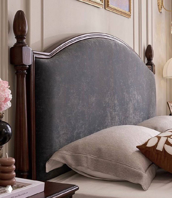 Детальный кадр мягкого изголовья кровати: обивка спокойного серого оттенка на фоне резных деревянных стоек из ясеня.