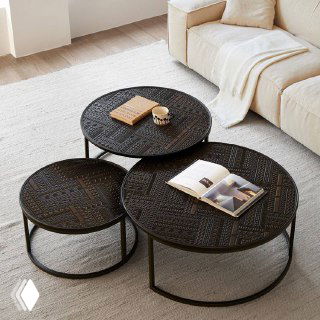 Три круглых журнальных столика тёмного цвета с рельефной поверхностью, на одном лежит книга и стоит кружка, фон — светлый диван.