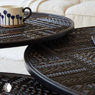 Фрагмент верхней поверхности двух соединённых столиков с чашкой на переднем плане — отделка и рисунок столешницы видны вблизи.