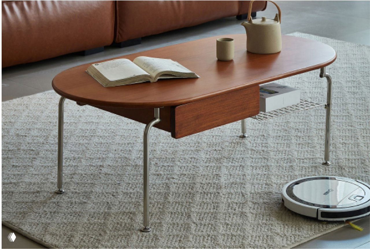 Журнальный столик из массива ясеня в интерьере: овальная столешница, хромированные ножки, книга и чашка на столе, рядом робот‑пылесос