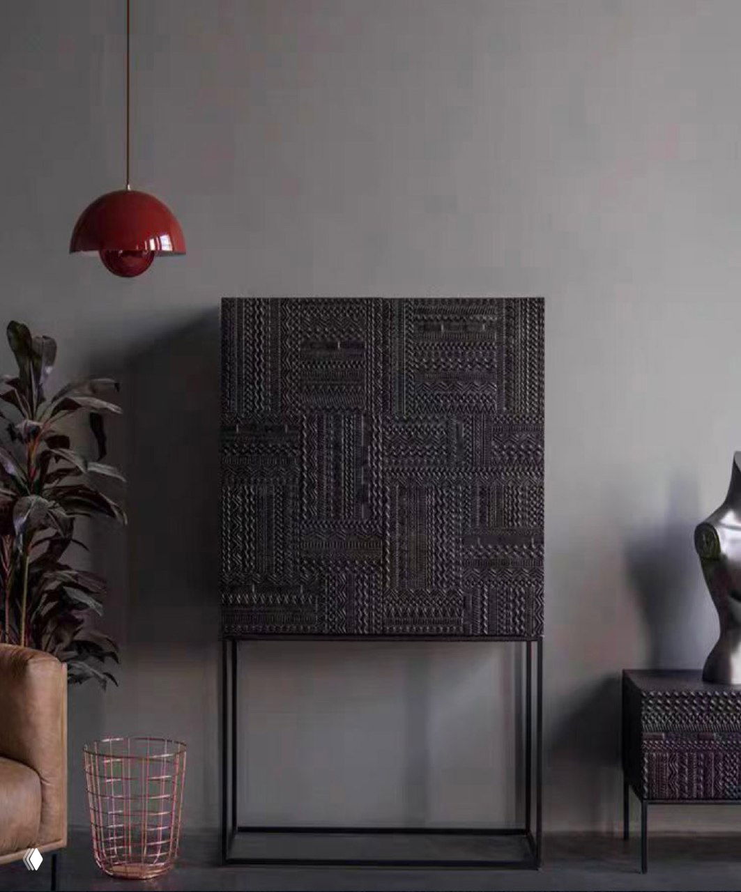 Темный шкаф из массива ясеня с рельефным фасадом на тонком металлическом основании в минималистичной гостиной, рядом кресло и подвесной светильник