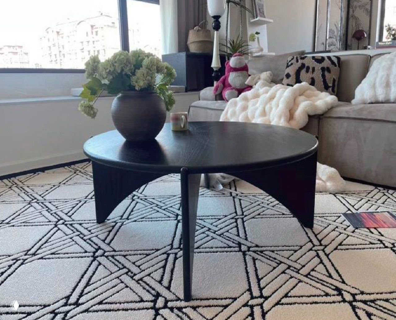 Круглый журнальный столик из темного ясеня в гостиной: стоит на узорном ковре возле дивана, на столе ваза с цветами.