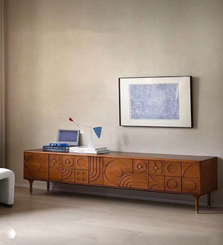 Тумба под ТВ из массива ясеня в светлом интерьере: резной фасад, низкие ножки, настольная лампа и картина на стене, демонстрация пропорций и стиля.