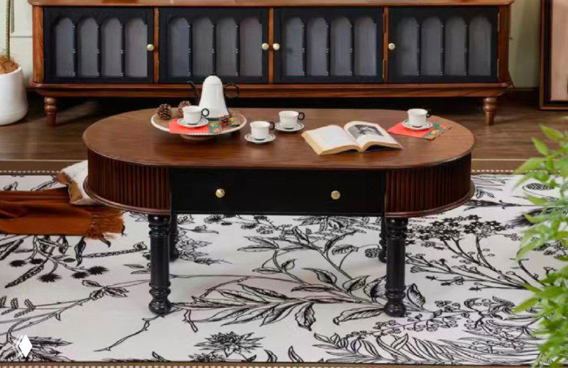 Овальный журнальный столик из массива ясеня в комнате: тёмные фигурные ножки, кружки и книга на столе, вид спереди.