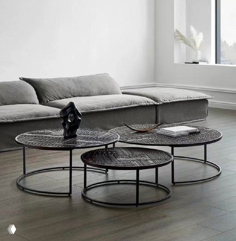 Три низких круглых журнальных столика с чёрной металлической рамой и плетёной столешницей в светлой гостиной.