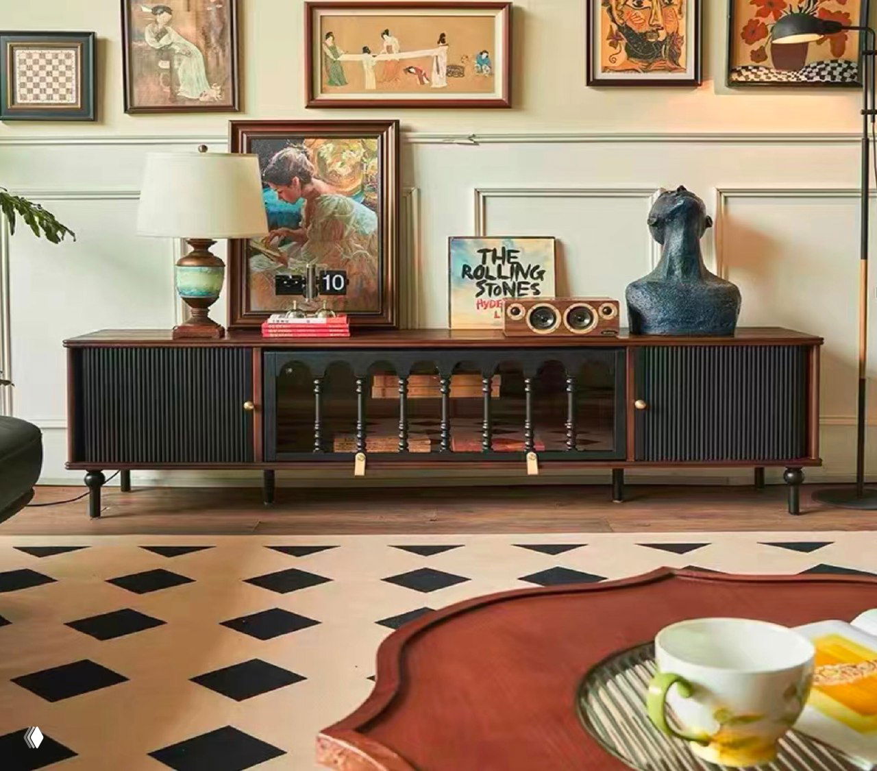 Тумба под телевизор из массива ясеня в оформленной гостиной: длинная тёмная тумба с лампой, картинами и декоративными предметами на верхней поверхности