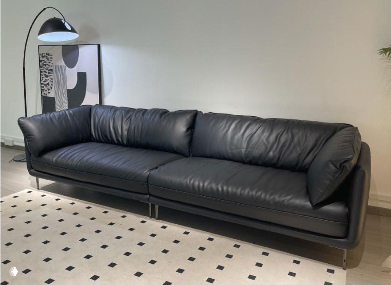 Черный кожаный трехместный диван в светлой гостиной на металлических ножках; вид спереди, мягкие съемные подушки и ровная обивка.