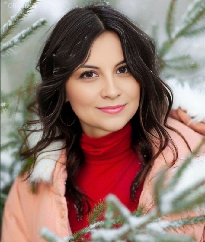 Портрет улыбающейся женщины в тёплой одежде на фоне еловых ветвей — зимнее, уютное праздничное настроение.