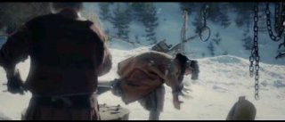 Кадр из экранизации «По щучьему велению»: зимний пейзаж, мужчина лежит на колоде, рядом фигуры в тёплой одежде и атмосферные детали сцены фильма.
