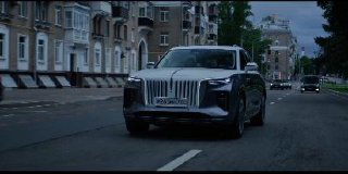 Кадр-превью: движущийся автомобиль по городской улице в пасмурную погоду, съёмка спереди‑слева, динамичная уличная сцена без людей.