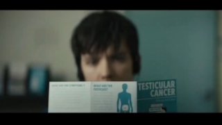 Кадр из фильма: размытый мужской персонаж держит брошюру про рак яичек в клиническом окружении — сцена, подчеркивающая тему страха за здоровье.