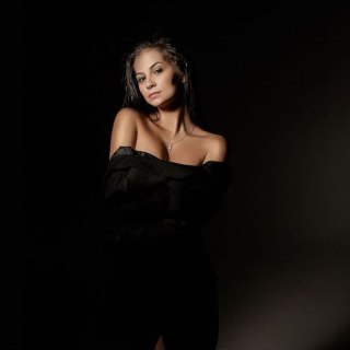 Студийный портрет взрослой женщины в чёрном открытом платье на тёмном фоне: психолог, задумчивый серьёзный взгляд, поза.