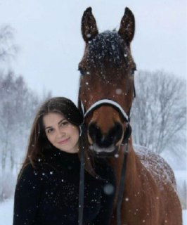 Женщина рядом с лошадью на заснеженной прогулке: на переднем плане лицо женщины и морда лошади, вокруг снег и деревья в зимнем пейзаже.