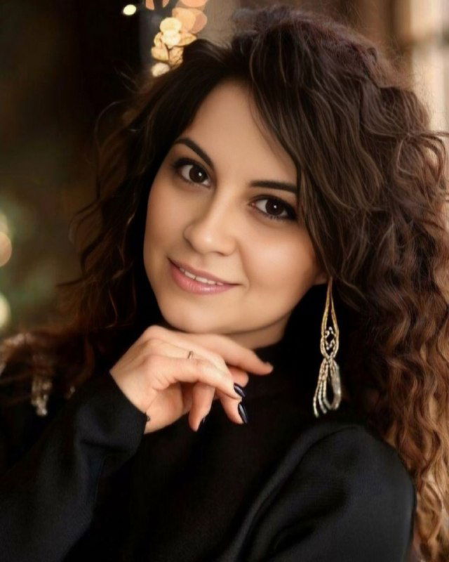 Студийный портрет улыбающейся женщины — автор канала, психолог Анастасия Копрова; тёмная одежда, завитые волосы, серьги.