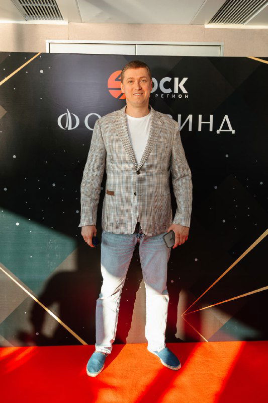 Фотография мужчины на красной дорожке у бренд-баннера с логотипом «Фордевинд», портретный кадр с деловой атмосферой мероприятия.