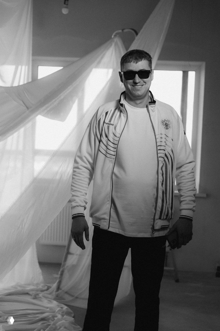 Портретный снимок одного из участников презентации на фоне декоративного паруса внутри демонстрационной зоны комплекса, чёрно‑белая стилизация.