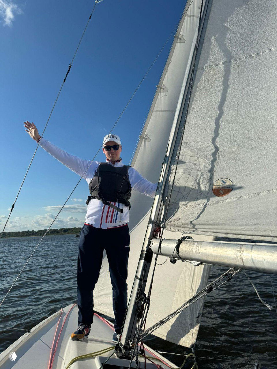 Участник презентации стоит на носу яхты рядом с парусом, раскинув руки, солнечный день и открытая вода на фоне — динамичный кадр с морем.