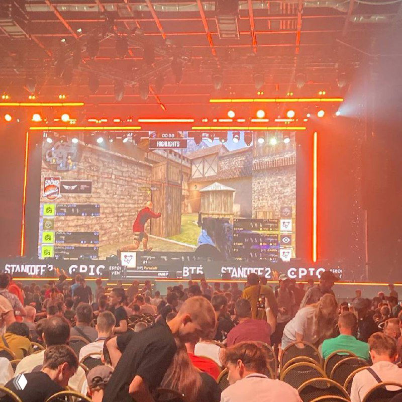 Большой экран с трансляцией матча StandOFF 2 и заполнённый зал зрителей: кадр со сценой, табло и разноцветная подсветка финала.