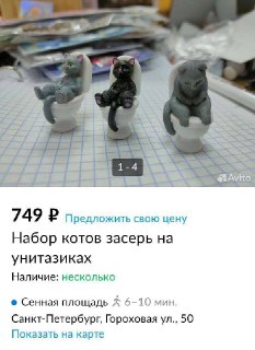 Фото трёх миниатюрных фигурок котов, сидящих на маленьких унитазах на клетчатой поверхности; на заднем плане видны стопки вещей и бумаги.
