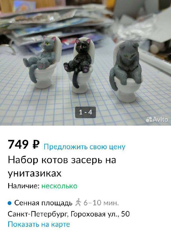 Три маленькие фигурки котов, каждая восседает на миниатюрном унитазе; фотография объявления сделана на столе.
