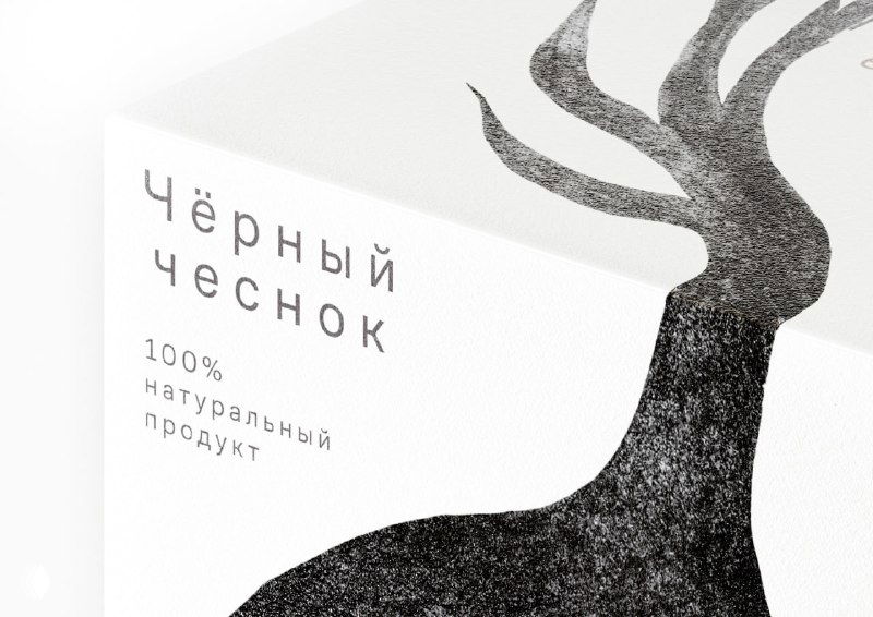 Крупный план белой упаковки чёрного чеснока с монохромной мрачной иллюстрацией в виде стилизованной чесночной головки