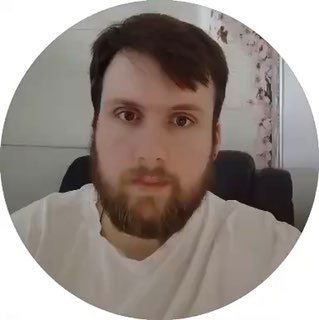 Круглый портрет: крупный план взрослого мужчины с бородой, светлая футболка, нейтральный интерьер и шторы на заднем плане, превью видео.