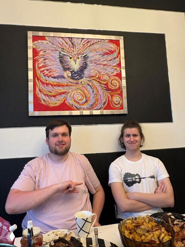 Два человека сидят за столом с тарелками и закусками, на стене позади них большая картина с птицей — иллюстрация учебно‑личной истории.