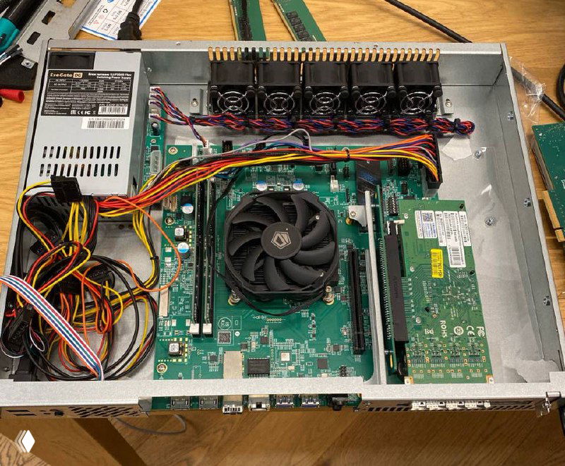 Вид внутренней компоновки прототипа маршрутизатора: плата с кулером, слоты памяти и плата интерфейсов в металлическом шасси на рабочем столе с кабелями и блоком питания.