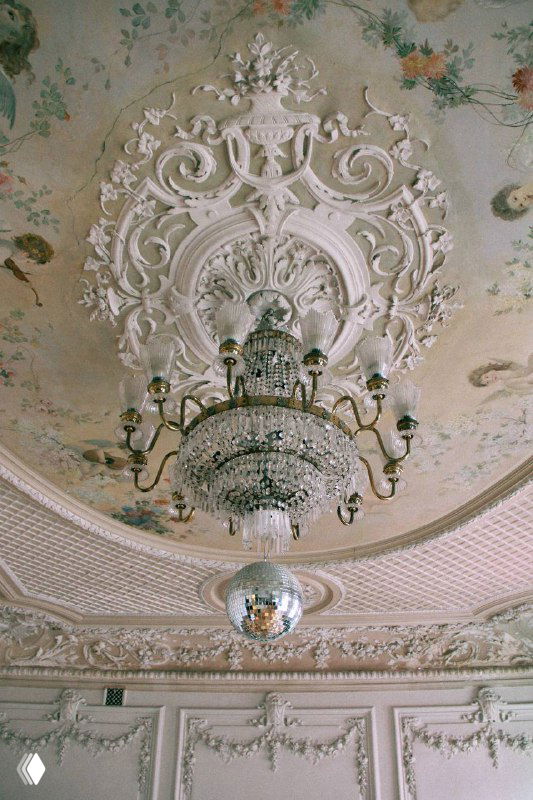 Деталь потолочной лепнины и хрустальная люстра в сочетании с зеркальным шаром — викторианская эстетика в интерьере особняка.