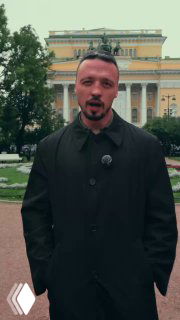 Человек в чёрном пальто на переднем плане на фоне большого неоклассического театрального здания в Санкт‑Петербурге, городской пейзаж.