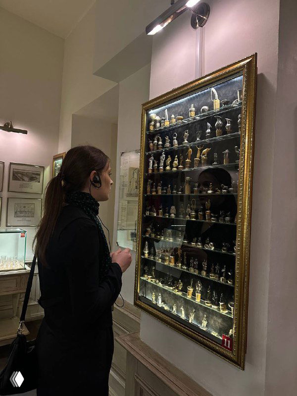 Посетительница рассматривает витрину с маленькими стеклянными флаконами и экспонатами, связанные с историей алкоголя и напитков.