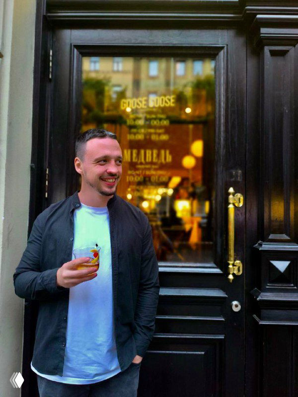 Человек у входной двери заведения с бокалом, отражение вывески и оформление входа «Медведь» — фасад и атмосфера на Большой Конюшенной.