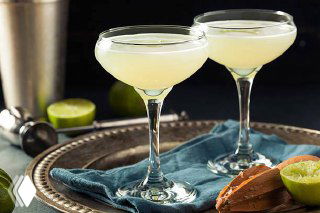 Два коктейля Gimlet в купе на подносе рядом с разрезанным лаймом и шейкером — светлая лимонно‑лаймовая подача в барной сервировке.