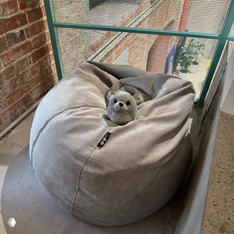 Серое кресло‑мешок у балконного окна с металлической сеткой; на нём маленькая мягкая игрушка в виде тюленя.