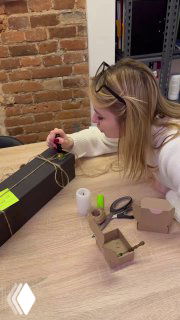 Крупный план: женщина накручивает украшение на коробку, рабочий стол с инструментами и материалами для упаковки подарков.