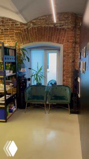 Интерьер офиса в историческом лофте: кирпичная кладка, окно, две мягкие кресла и стеллаж с папками — уютный рабочий угол компании.