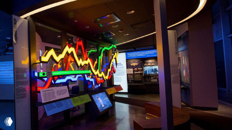 Инсталляция с разноцветными графиками и интерактивными панелями, показывающая исторические колебания курса валют в экономическом контексте.