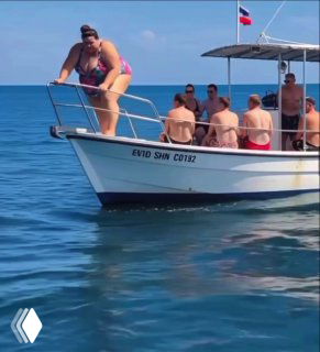 Группа людей на прогулочном катере в спокойном море; видна носовая часть лодки, несколько отдыхающих и флаг на корме.