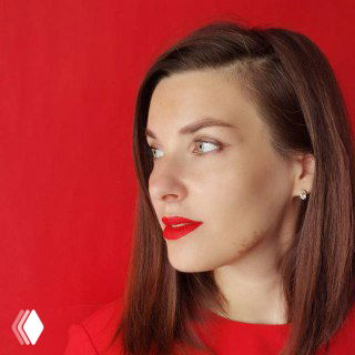 Портрет женщины в профиль на ярко‑красном фоне: светлая кожа, коричневые волосы, красная помада; деловой образ, плечи видны, студийная съёмка.